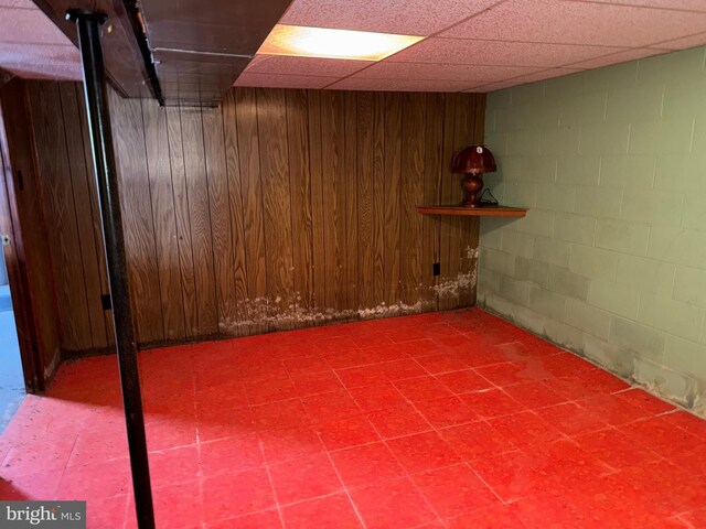 basement with a paneled ceiling and wood walls