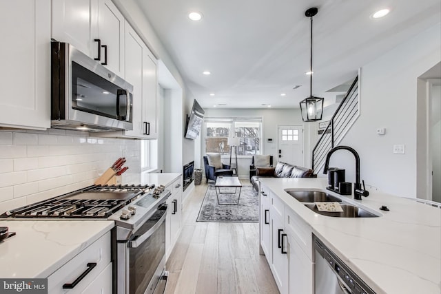 kitchen with white cabinetry, stainless steel appliances, sink, and hanging light fixtures