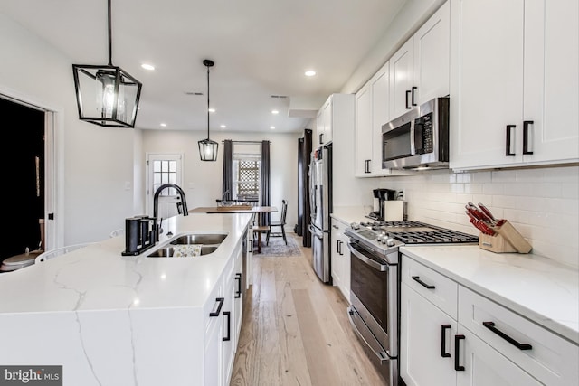 kitchen featuring sink, hanging light fixtures, stainless steel appliances, a kitchen island with sink, and white cabinets