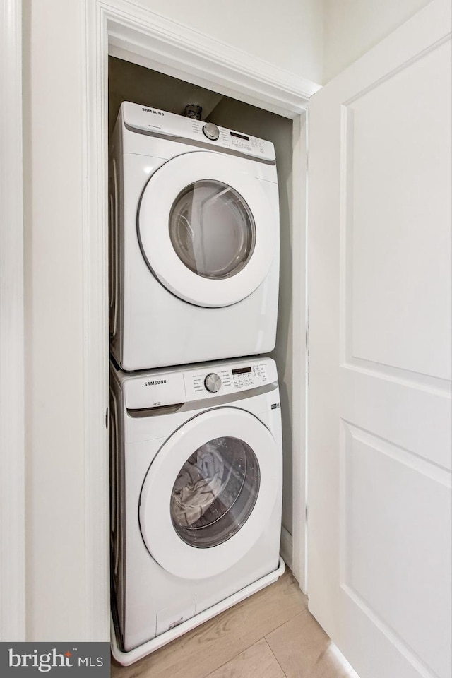 laundry room featuring stacked washer / drying machine and light hardwood / wood-style flooring