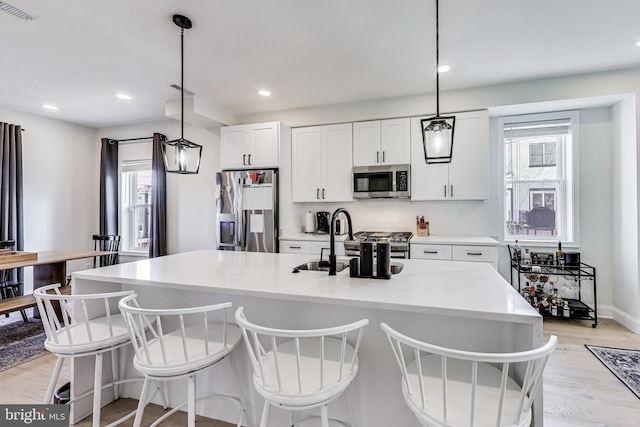 kitchen featuring stainless steel appliances, white cabinetry, hanging light fixtures, and a kitchen island with sink