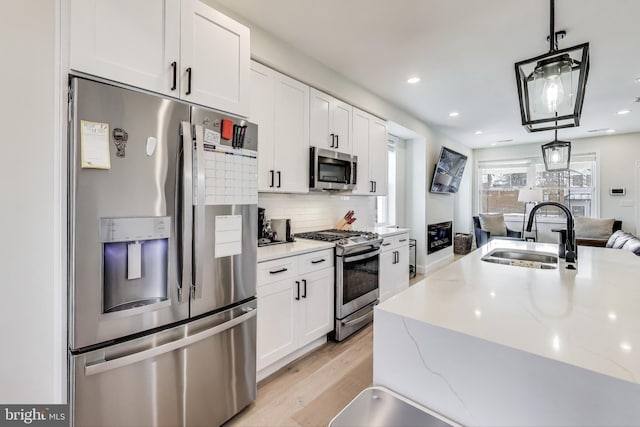 kitchen featuring stainless steel appliances, sink, pendant lighting, and white cabinets