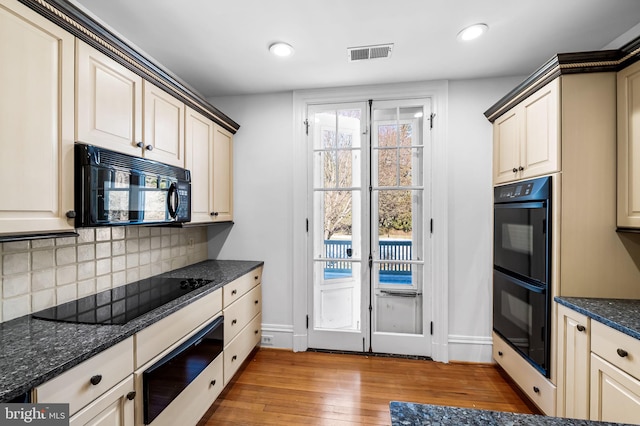 kitchen with light hardwood / wood-style flooring, dark stone countertops, tasteful backsplash, black appliances, and cream cabinetry