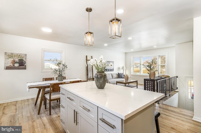 kitchen featuring a kitchen island, decorative light fixtures, a kitchen breakfast bar, light stone countertops, and light hardwood / wood-style flooring