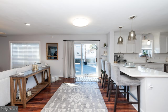 kitchen featuring dark hardwood / wood-style floors, pendant lighting, white cabinetry, sink, and a kitchen breakfast bar