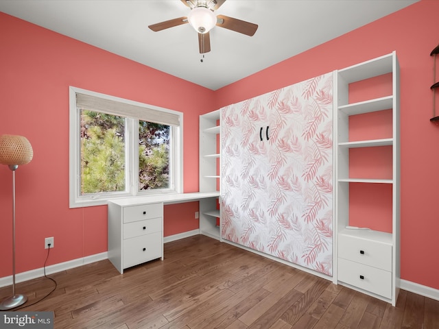 unfurnished office featuring hardwood / wood-style floors, built in desk, and ceiling fan