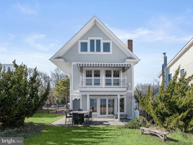 rear view of house with french doors, a balcony, a patio, and a lawn