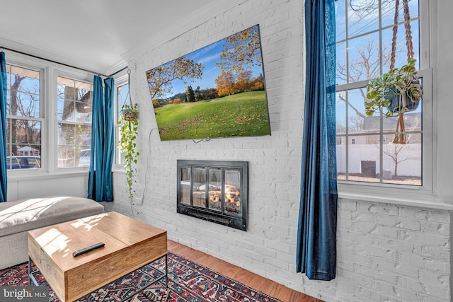 living room with hardwood / wood-style flooring, ornamental molding, brick wall, and a brick fireplace