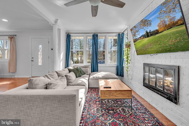 living room featuring ornate columns, wood-type flooring, a brick fireplace, and ceiling fan