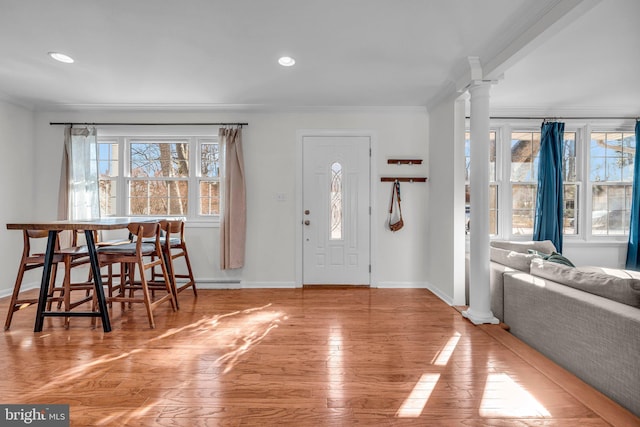 entrance foyer with crown molding, light hardwood / wood-style flooring, a healthy amount of sunlight, and ornate columns