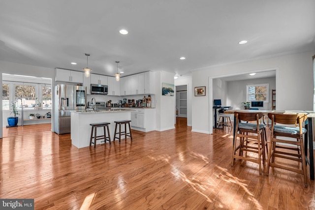 kitchen with white cabinetry, stainless steel appliances, a kitchen island with sink, and pendant lighting