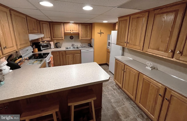 kitchen featuring sink, white appliances, a breakfast bar area, and kitchen peninsula