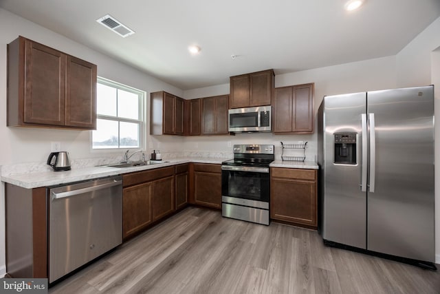 kitchen featuring stainless steel appliances, sink, dark brown cabinetry, and light hardwood / wood-style flooring