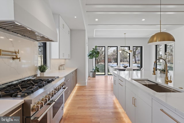 kitchen with sink, custom exhaust hood, pendant lighting, range with two ovens, and white cabinets