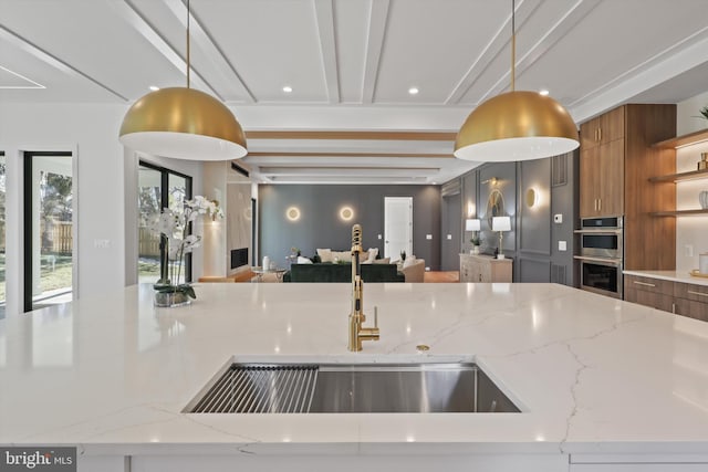 kitchen with light stone counters, stainless steel double oven, sink, and pendant lighting