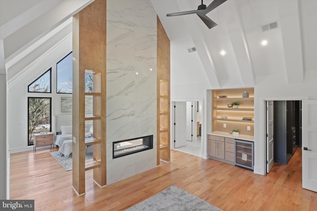 living room featuring beverage cooler, a premium fireplace, beam ceiling, and light hardwood / wood-style flooring