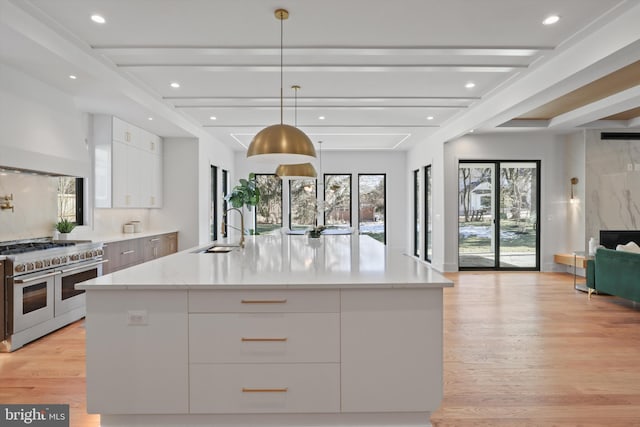 kitchen with decorative light fixtures, sink, white cabinets, range with two ovens, and a large island