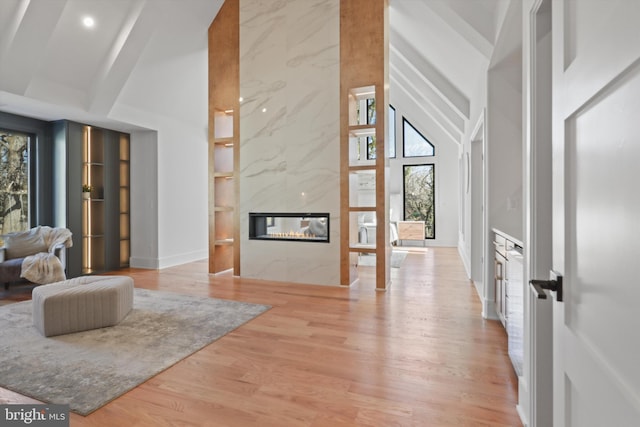 living room featuring a healthy amount of sunlight, a high end fireplace, high vaulted ceiling, and light hardwood / wood-style floors