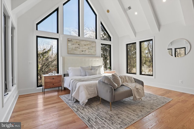 bedroom with multiple windows, high vaulted ceiling, light wood-type flooring, and beam ceiling