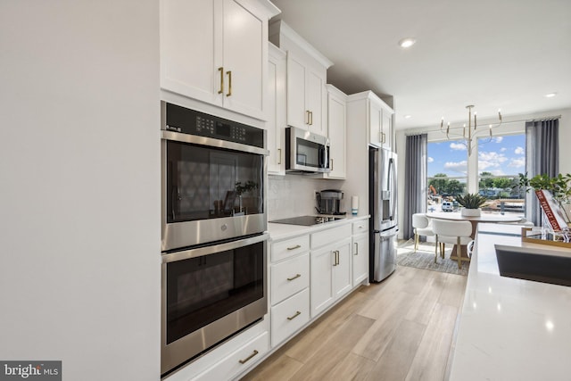 kitchen with white cabinetry, backsplash, an inviting chandelier, stainless steel appliances, and light wood-type flooring