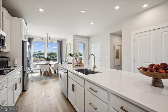 kitchen featuring pendant lighting, sink, stainless steel appliances, light stone countertops, and white cabinets