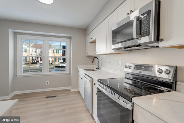 kitchen with appliances with stainless steel finishes, sink, white cabinets, light hardwood / wood-style floors, and light stone countertops