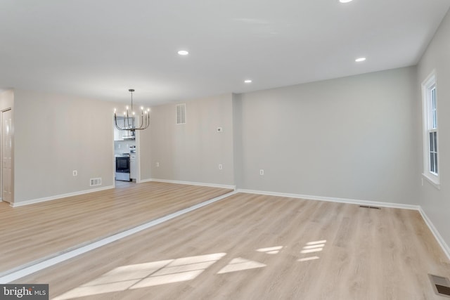 unfurnished living room featuring an inviting chandelier and light hardwood / wood-style flooring