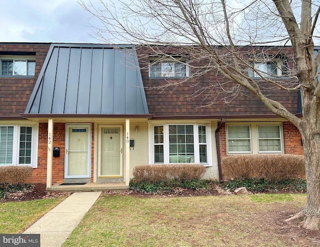 townhome / multi-family property with a standing seam roof, brick siding, a shingled roof, and metal roof