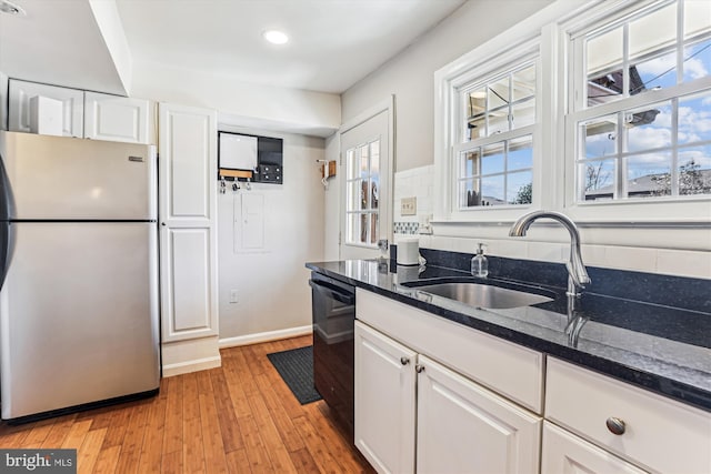 kitchen with dishwashing machine, dark stone countertops, freestanding refrigerator, white cabinets, and a sink