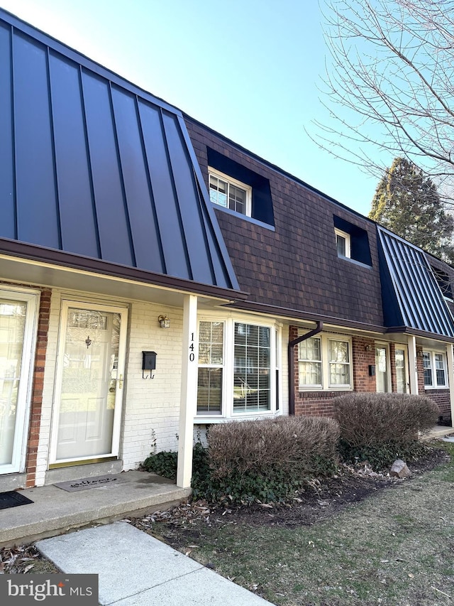 multi unit property with brick siding, mansard roof, and a shingled roof