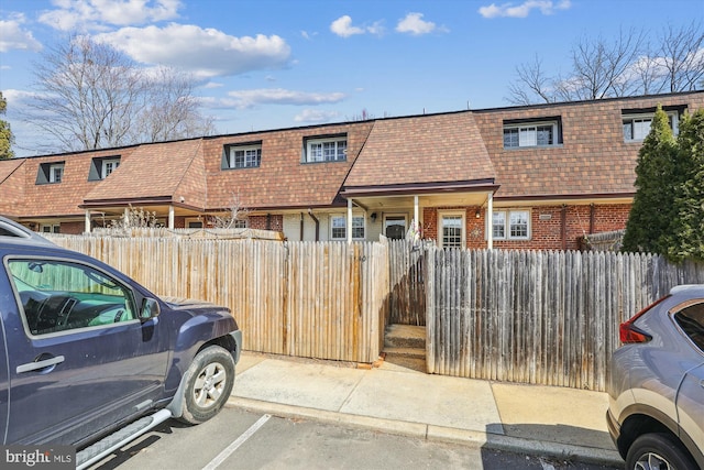 view of property featuring roof with shingles, mansard roof, uncovered parking, a fenced front yard, and brick siding