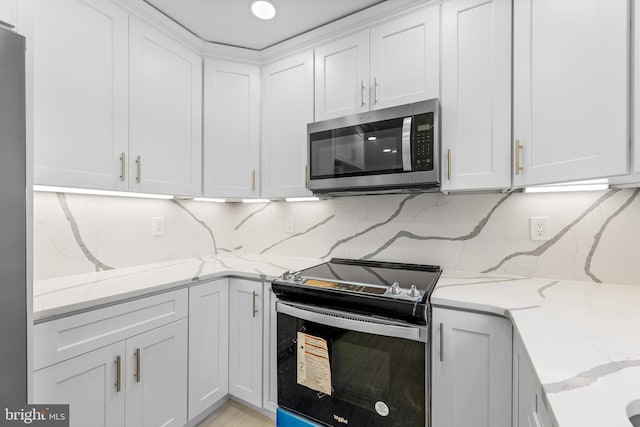 kitchen with stainless steel appliances, white cabinetry, light stone countertops, and decorative backsplash