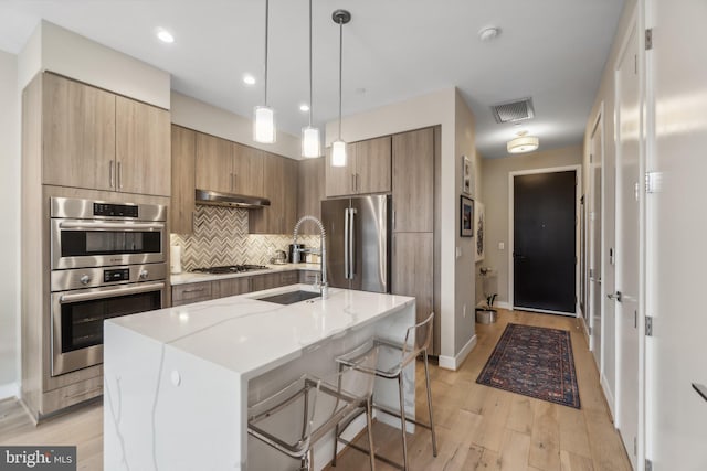 kitchen featuring sink, a center island with sink, appliances with stainless steel finishes, a kitchen breakfast bar, and light stone countertops