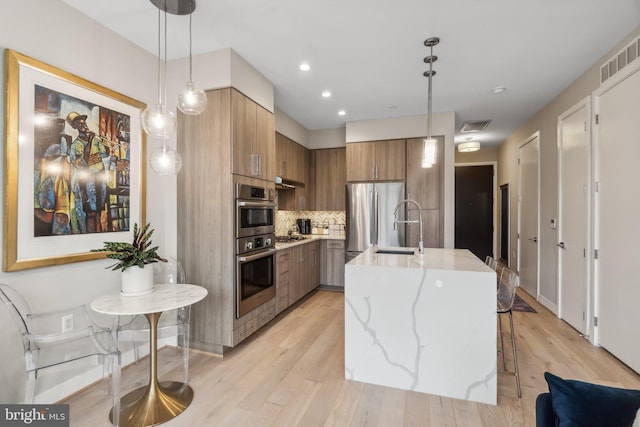 kitchen with a center island with sink, appliances with stainless steel finishes, a kitchen breakfast bar, pendant lighting, and light hardwood / wood-style floors