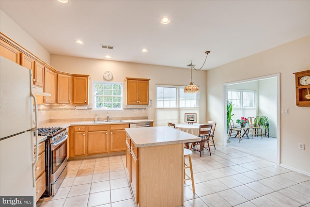 kitchen featuring sink, stainless steel gas range oven, decorative light fixtures, a center island, and white refrigerator