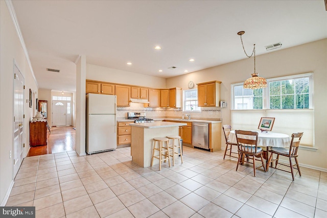 kitchen with light tile patterned floors, stainless steel appliances, tasteful backsplash, a kitchen island, and decorative light fixtures