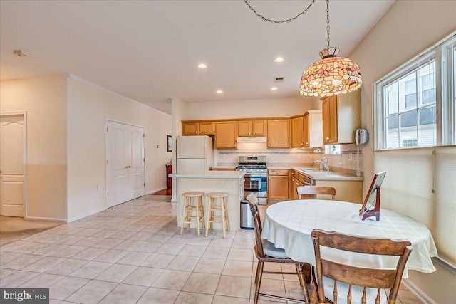 kitchen with pendant lighting, sink, white fridge, light tile patterned floors, and stainless steel range with gas stovetop