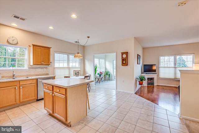 kitchen with sink, light tile patterned floors, dishwasher, a kitchen island, and pendant lighting