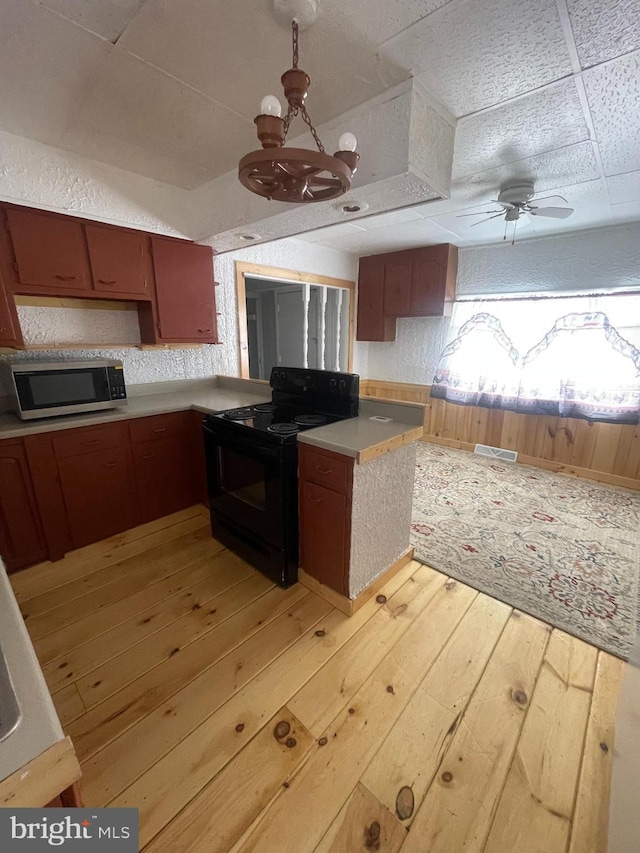 kitchen featuring ceiling fan with notable chandelier, a drop ceiling, black electric range, and light wood-type flooring