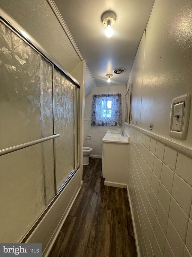 full bathroom with toilet, combined bath / shower with glass door, wood-type flooring, tile walls, and vanity