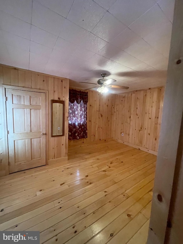 interior space featuring wood-type flooring, wooden walls, and ceiling fan