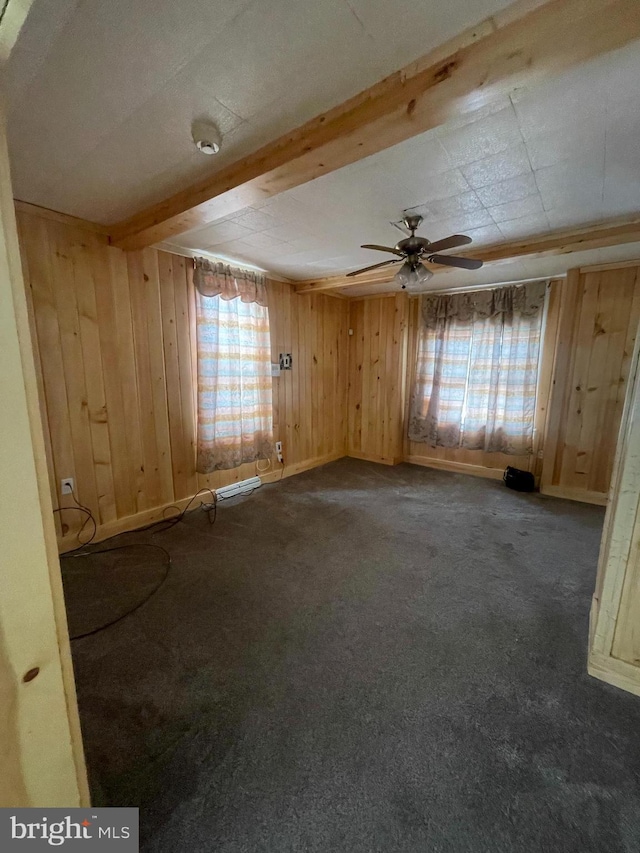 carpeted empty room featuring ceiling fan, wooden walls, beamed ceiling, and a healthy amount of sunlight