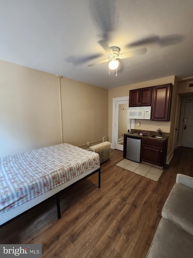 bedroom with ceiling fan, radiator heating unit, sink, and light hardwood / wood-style flooring