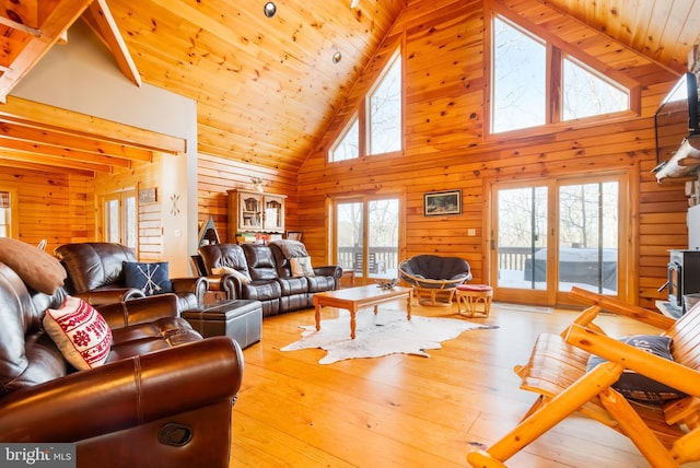 living room featuring wood ceiling, high vaulted ceiling, light hardwood / wood-style flooring, a wood stove, and wooden walls