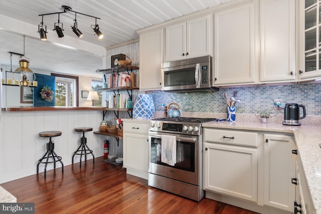 kitchen with dark wood-type flooring, appliances with stainless steel finishes, light stone countertops, and tasteful backsplash