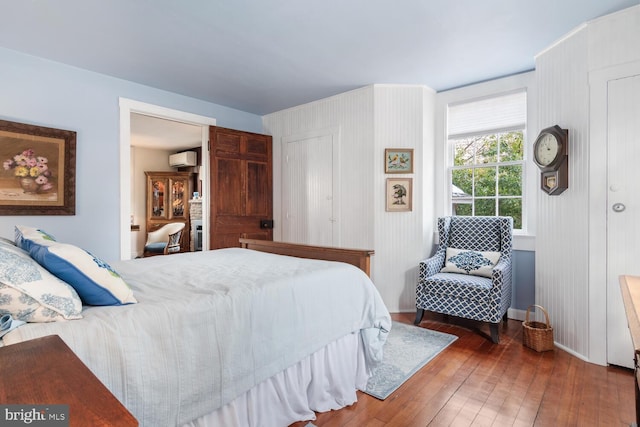 bedroom with dark hardwood / wood-style flooring and an AC wall unit