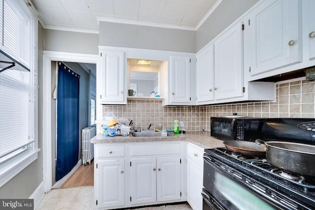 kitchen featuring sink, radiator heating unit, black appliances, ornamental molding, and white cabinets