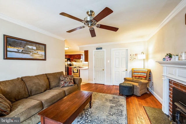 living room featuring a brick fireplace, ornamental molding, ceiling fan, and light wood-type flooring