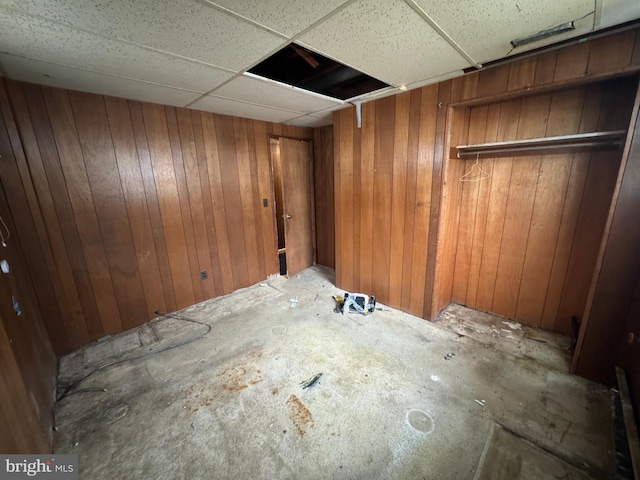 basement featuring a drop ceiling and wood walls