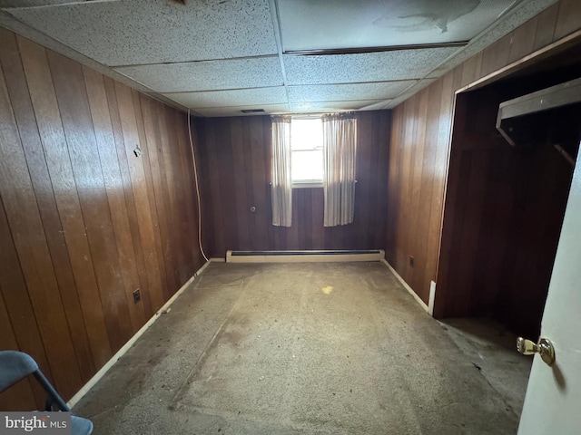 spare room featuring a baseboard heating unit, a drop ceiling, and wood walls